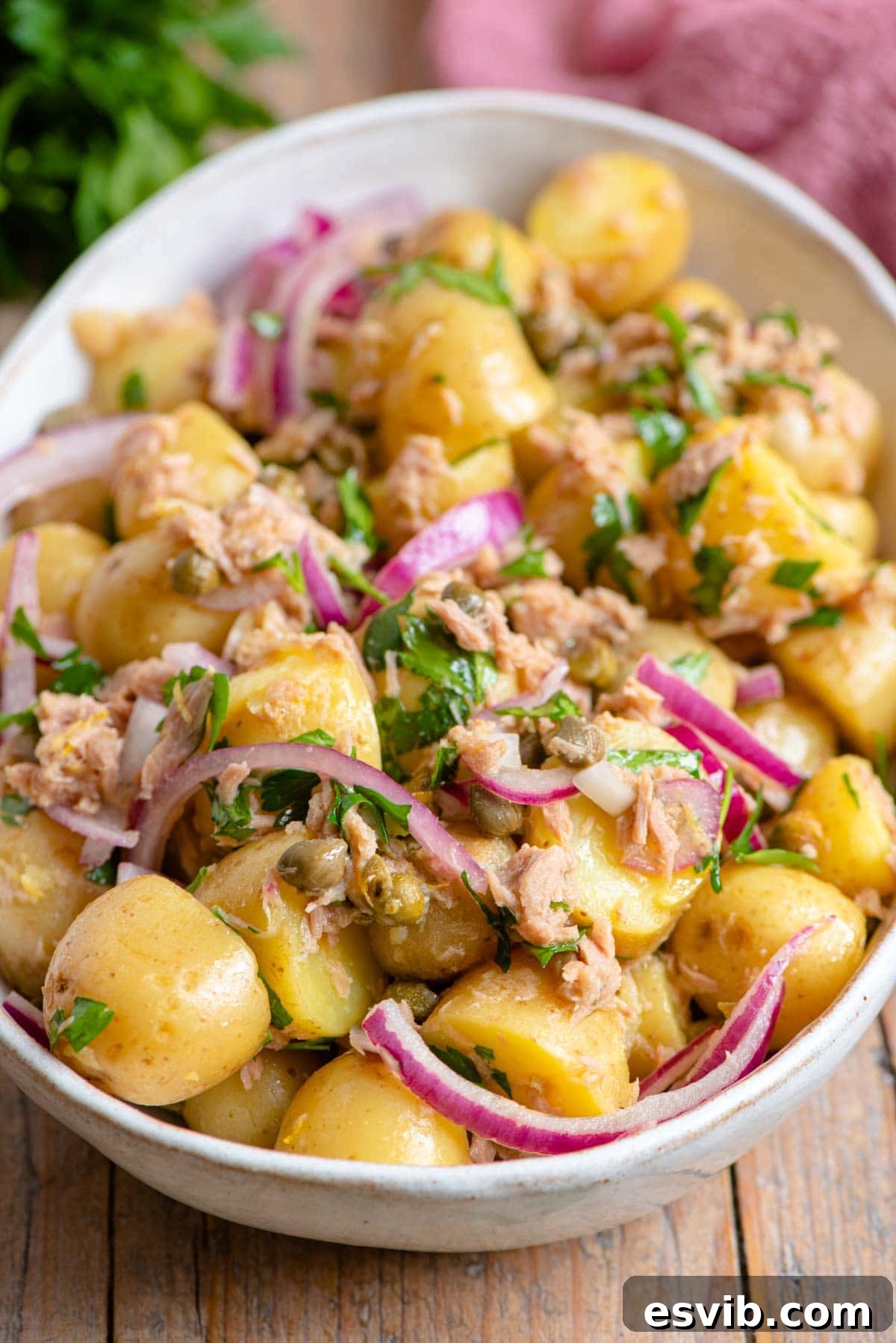 A close up of a vibrant Italian Tuna Potato Salad in a bowl, featuring visible red onion slices and capers.