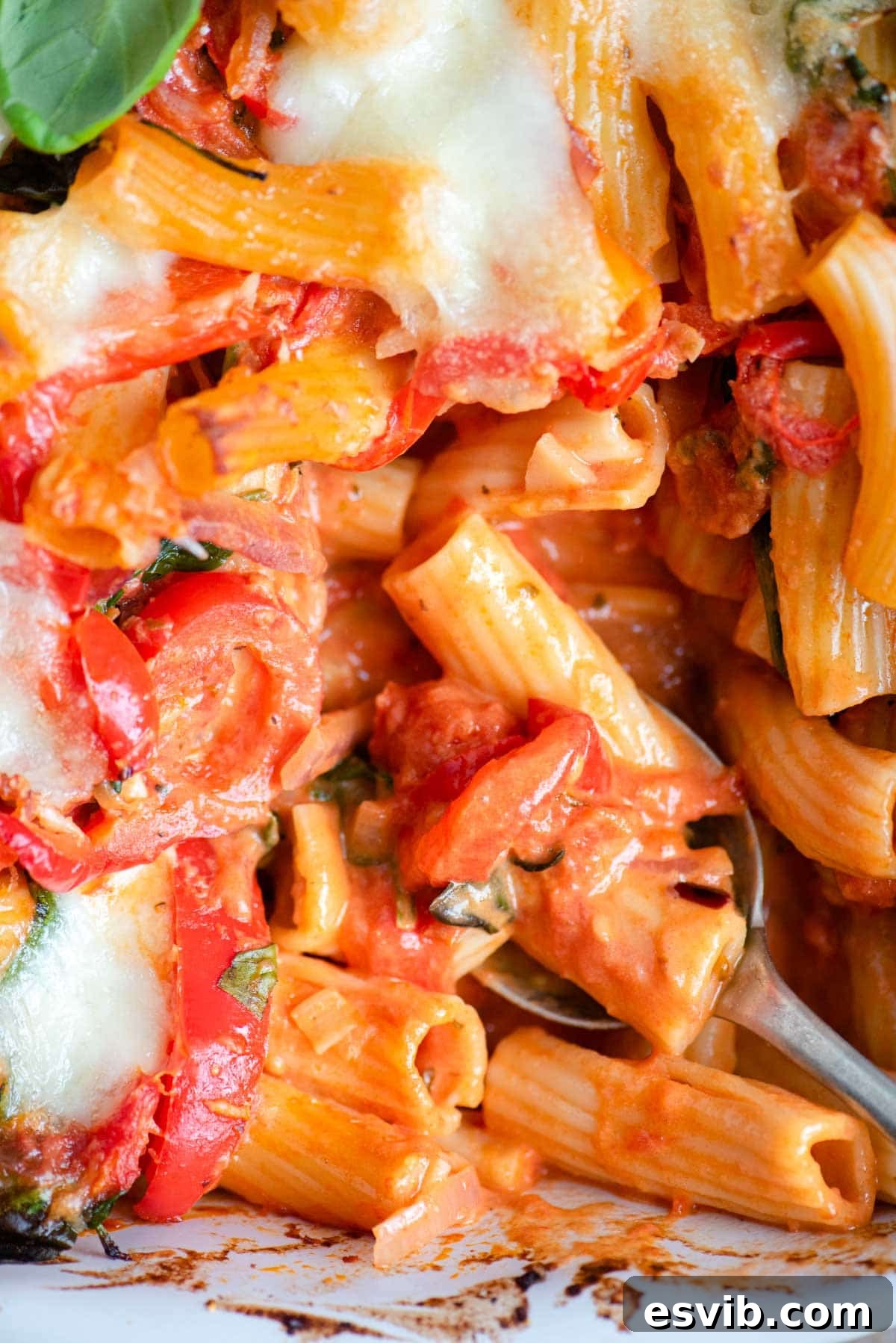 A close up of baked ziti with vegetables in a rich tomato sauce and melted cheese, ready to be enjoyed