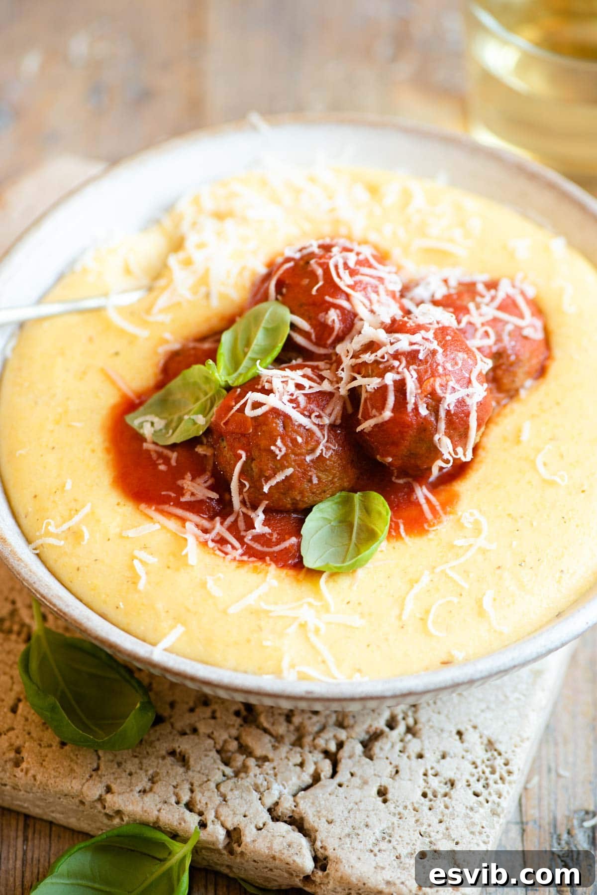 Plant-Based Eggplant Meatballs in Rustic Tomato Sauce 2 Eggplant meatballs in tomato sauce sitting on top of a bowl of polenta, garnished with fresh basil.
