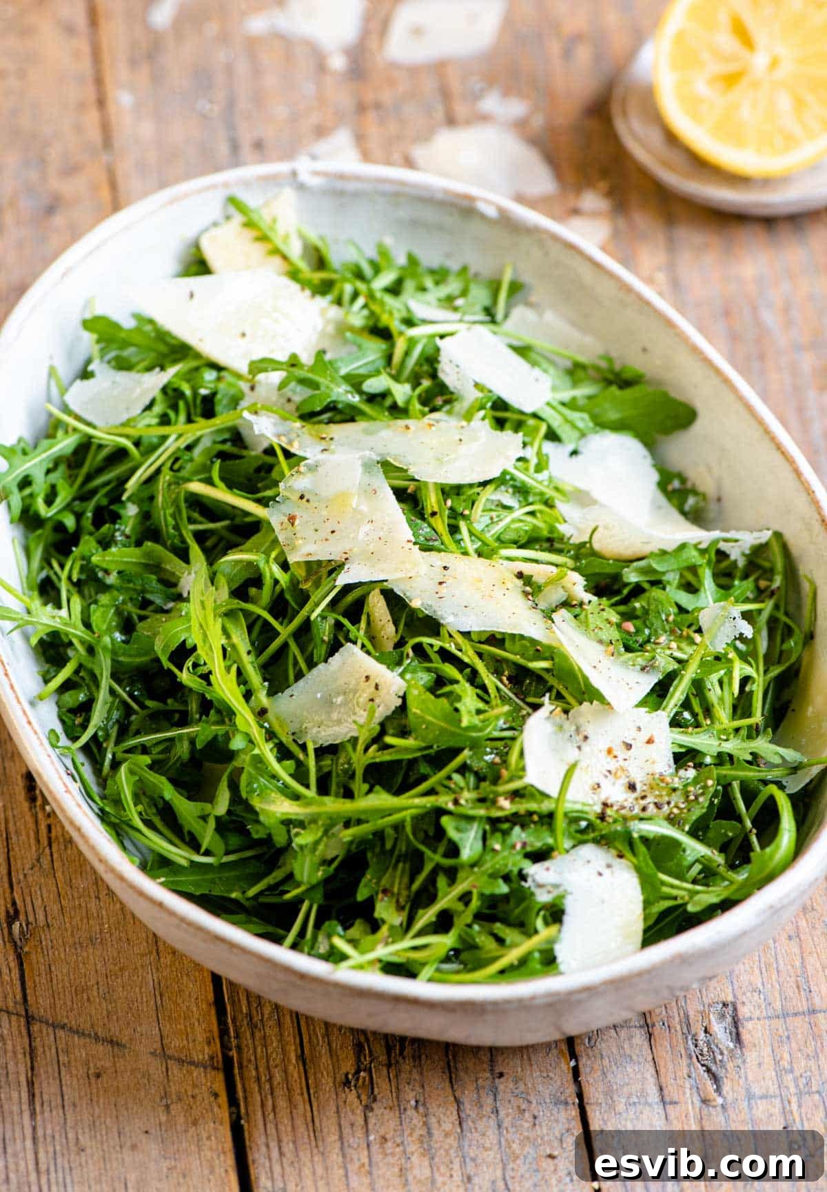 A vibrant arugula salad in a large serving bowl with generous shavings of parmesan
