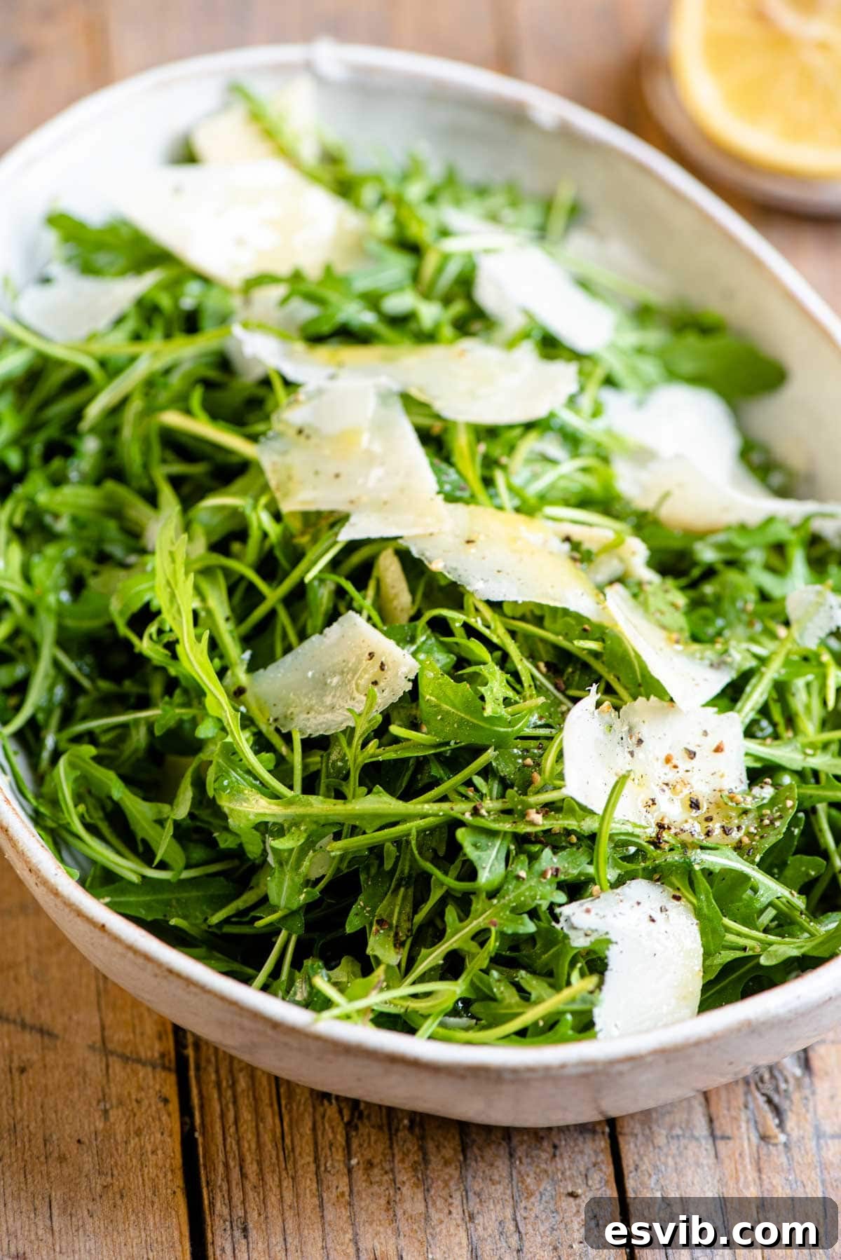 A close-up of a vibrant arugula salad glistening with dressing and topped with parmesan shavings in a rustic bowl