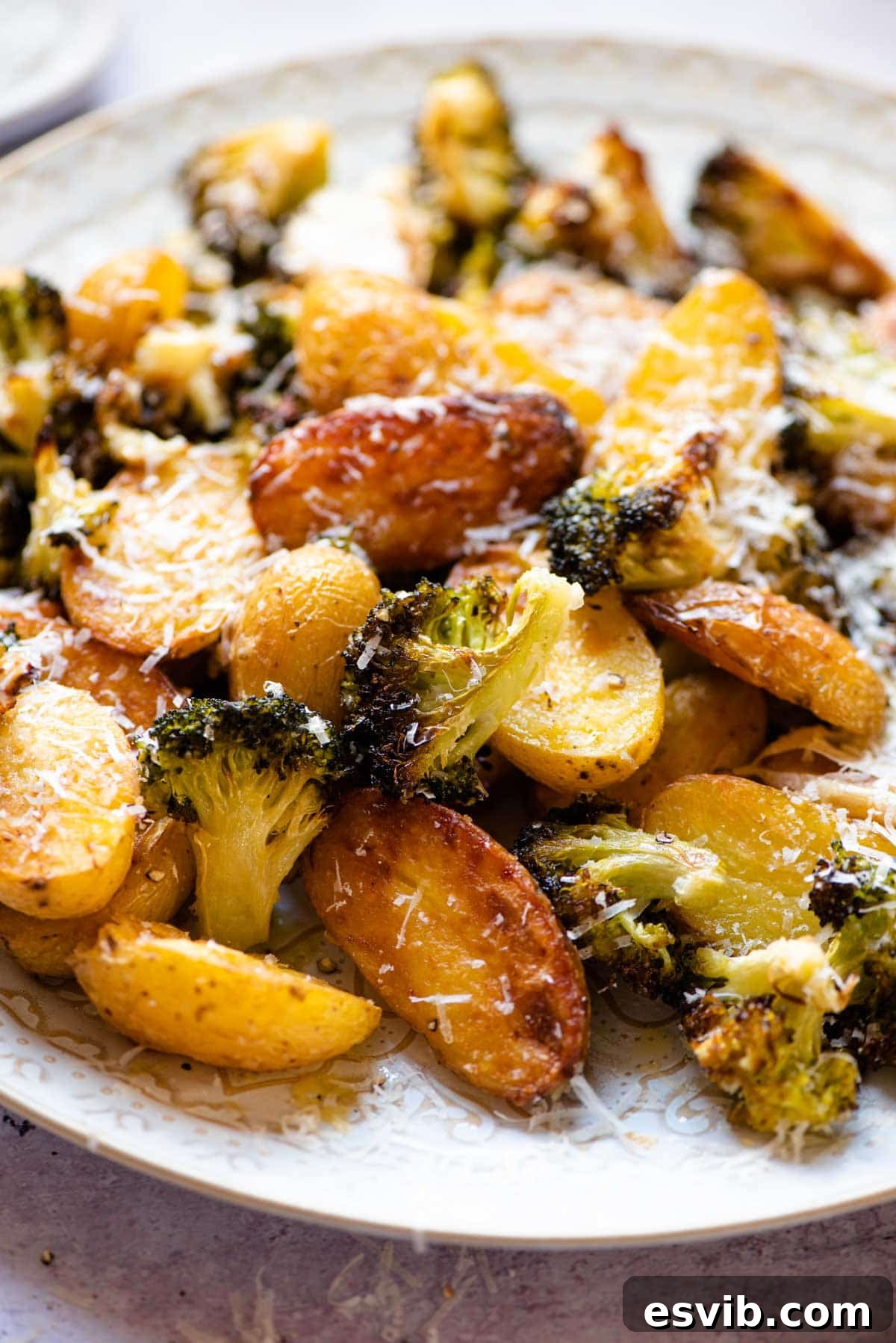A close-up view of the finished roasted potatoes and broccoli on a baking sheet, showing golden-brown potatoes, charred broccoli, and sweet roasted garlic, all tossed with melted parmesan cheese.
