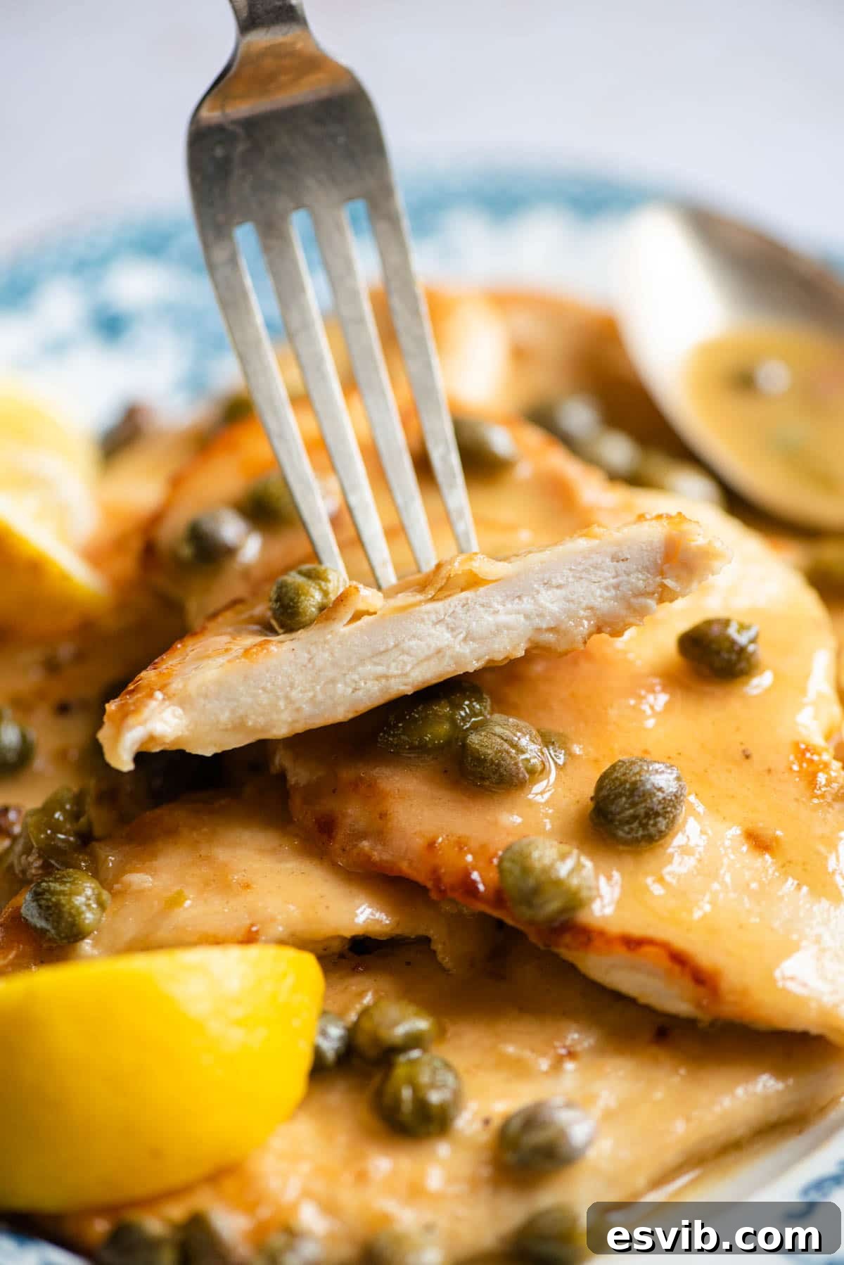 Zesty Lemon Caper Chicken Piccata 6 A close-up shot of a single piece of perfectly cooked Chicken Piccata on a fork, showing the tender chicken and glistening sauce.