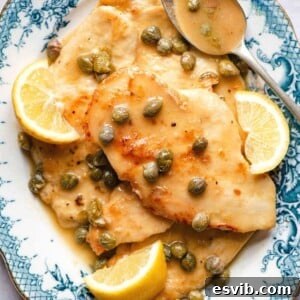 Zesty Lemon Caper Chicken Piccata 7 A close up of chicken piccata on a blue plate, garnished with fresh lemon and capers.