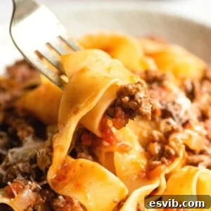 A close-up of lamb ragu and pappardelle pasta on a fork, ready to be eaten.