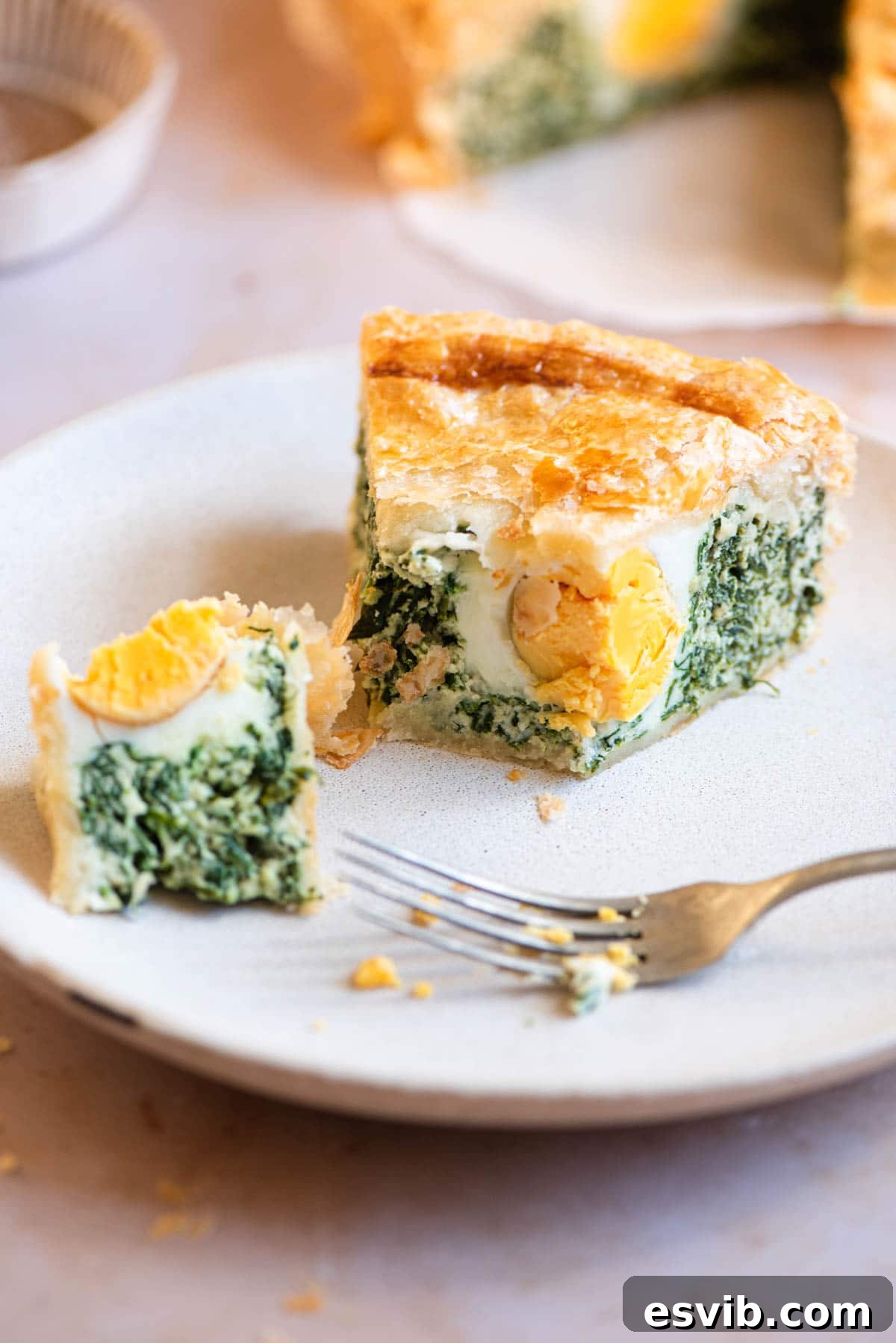 Torta Pasqualina Savory Spinach and Ricotta Easter Pie 7 A perfectly portioned slice of Torta Pasqualina artfully presented on a plate, cut in half to showcase its exquisite interior with a visible cooked egg.