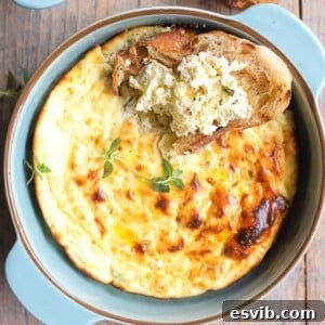 A close up cropped square image of baked ricotta in a blue ceramic round dish topped with a slice of crusty bread dipped in