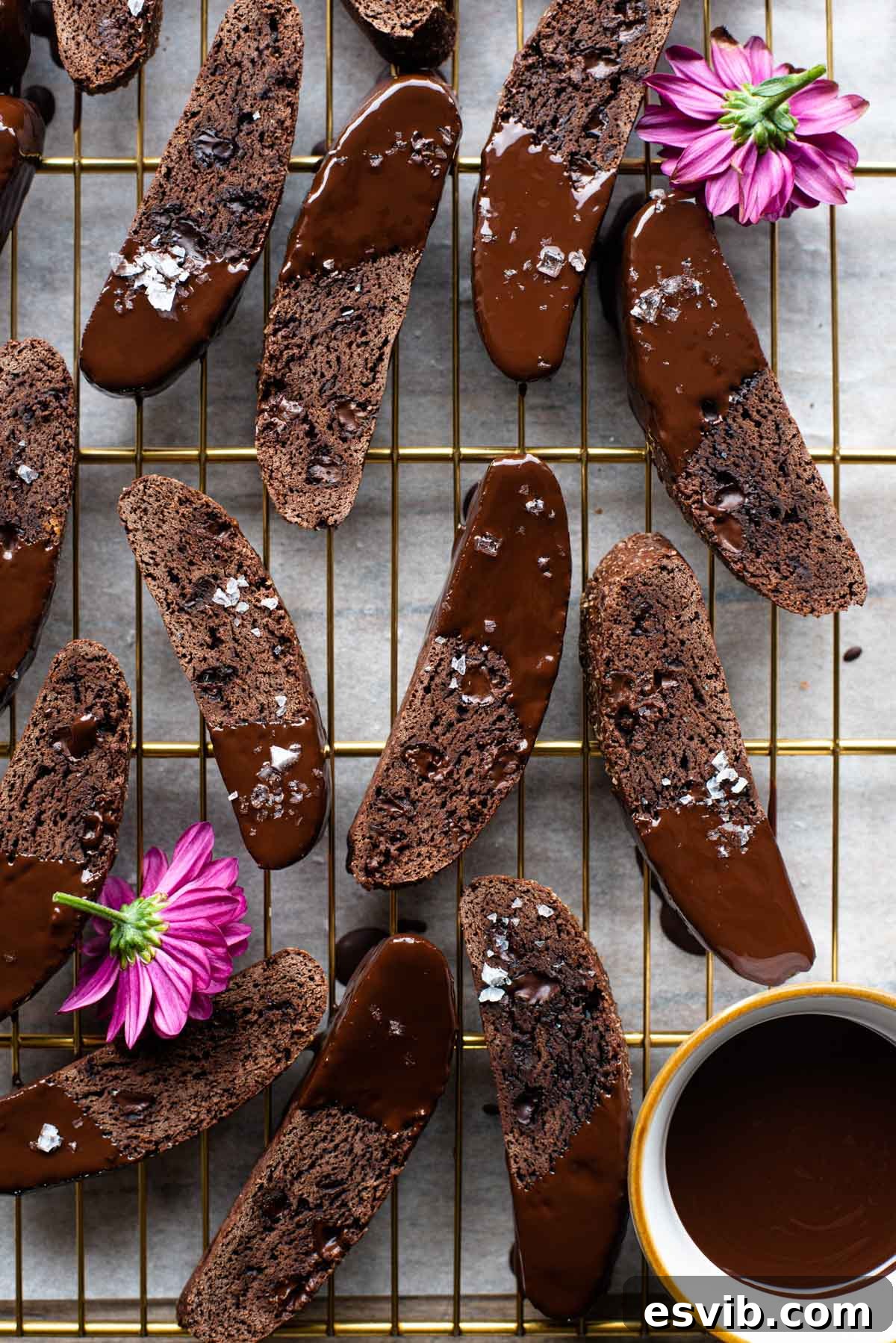 An overhead shot of chocolate biscotti on a cooling rack, showcasing their rich, dark color and irregular shapes from being twice-baked. Some are dipped in chocolate, while others are plain.