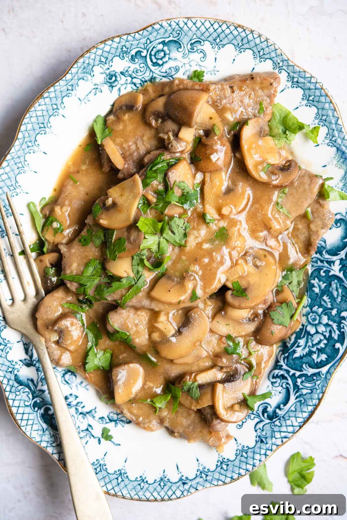 An overhead shot of authentic Veal Marsala served on a blue platter with sautéed mushrooms and fresh parsley garnish