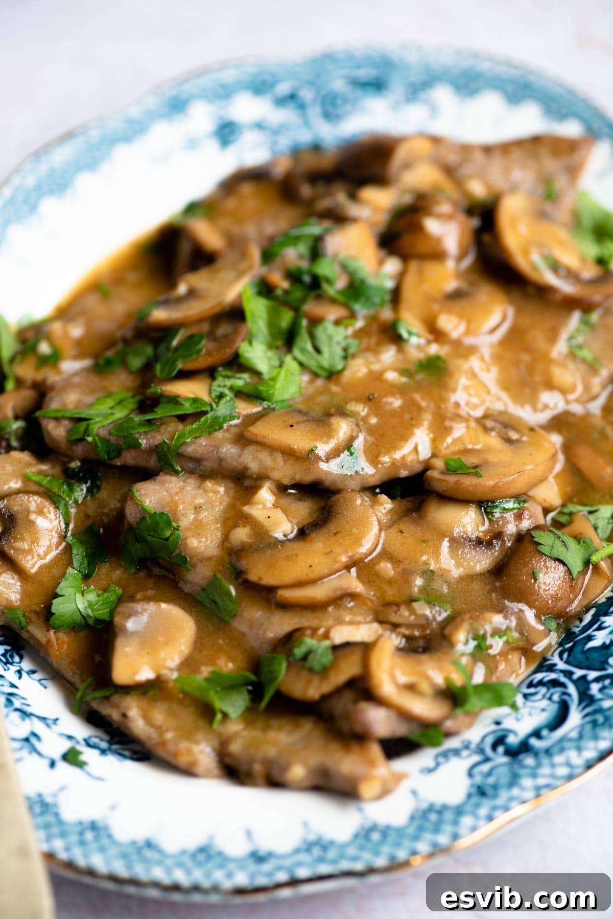 A close-up shot of rich and saucy Veal Marsala, garnished with mushrooms and fresh parsley, ready to be served
