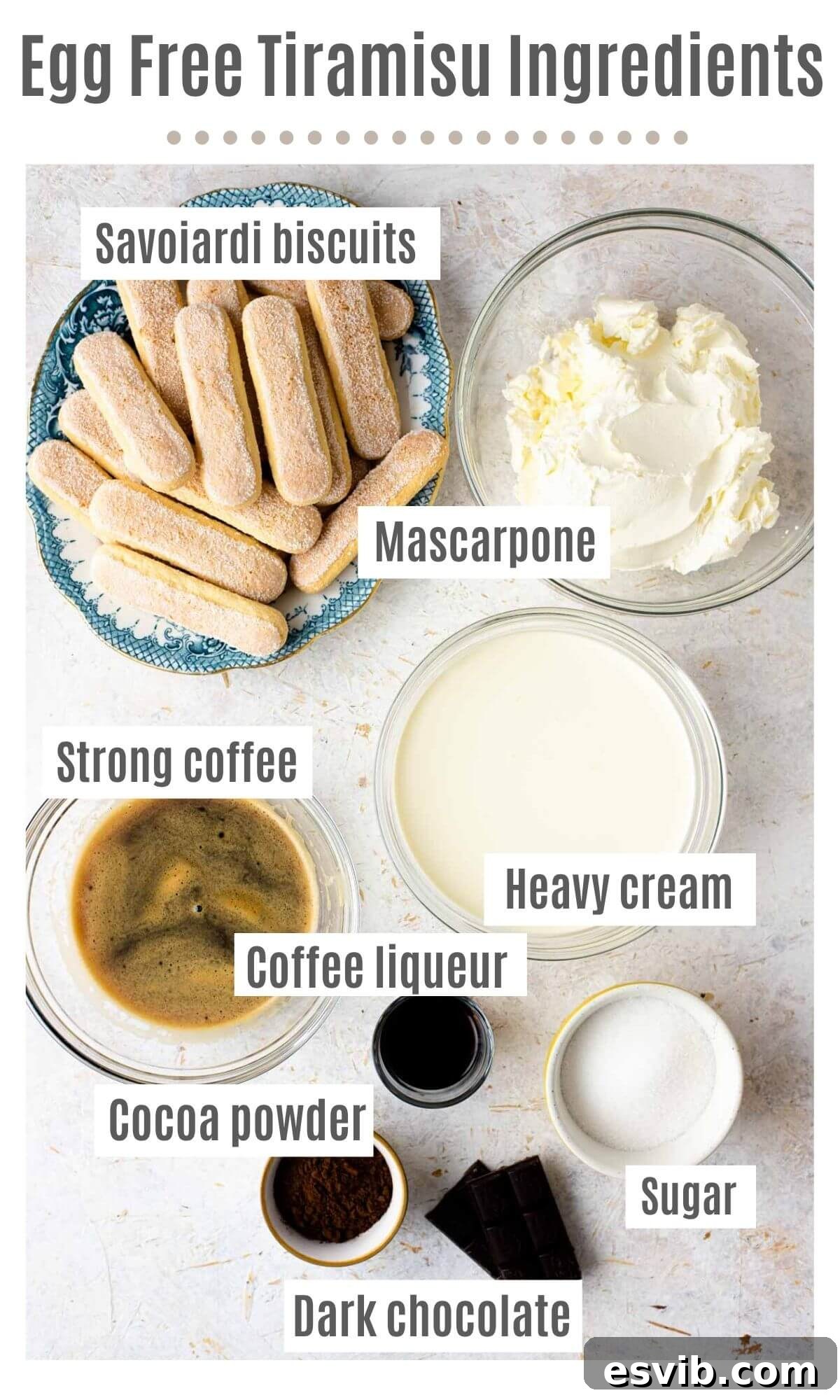 An overhead shot of all the key ingredients neatly arranged for making egg-free tiramisu, including Savoiardi biscuits, mascarpone, heavy cream, sugar, espresso, coffee liqueur, and cocoa powder.