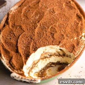 A close-up shot of a dish of Eggless Tiramisu with a slice already removed, highlighting its creamy layers.