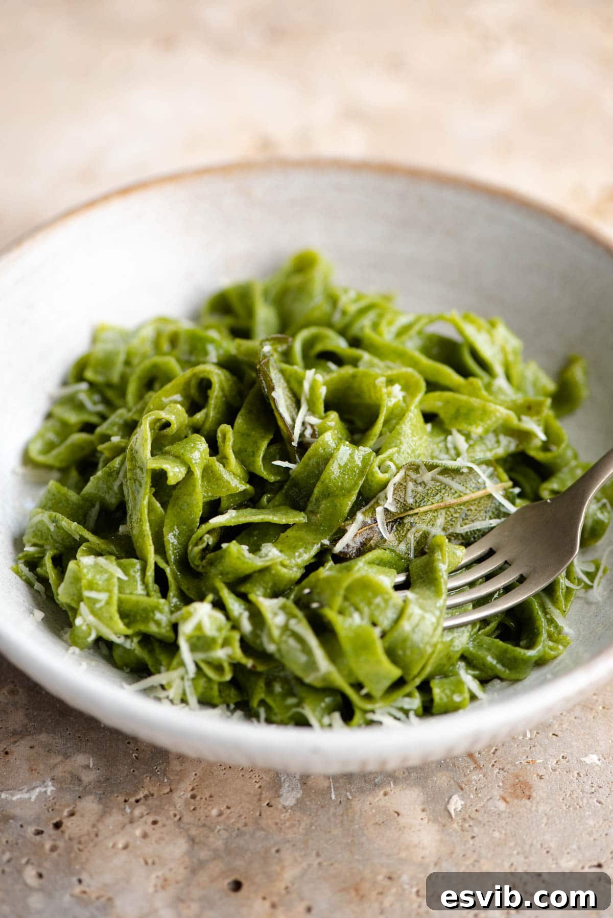 A close up shot of vibrant green, cooked spinach pasta, gently tossed in a bowl, highlighting its appealing color and delicious texture.
