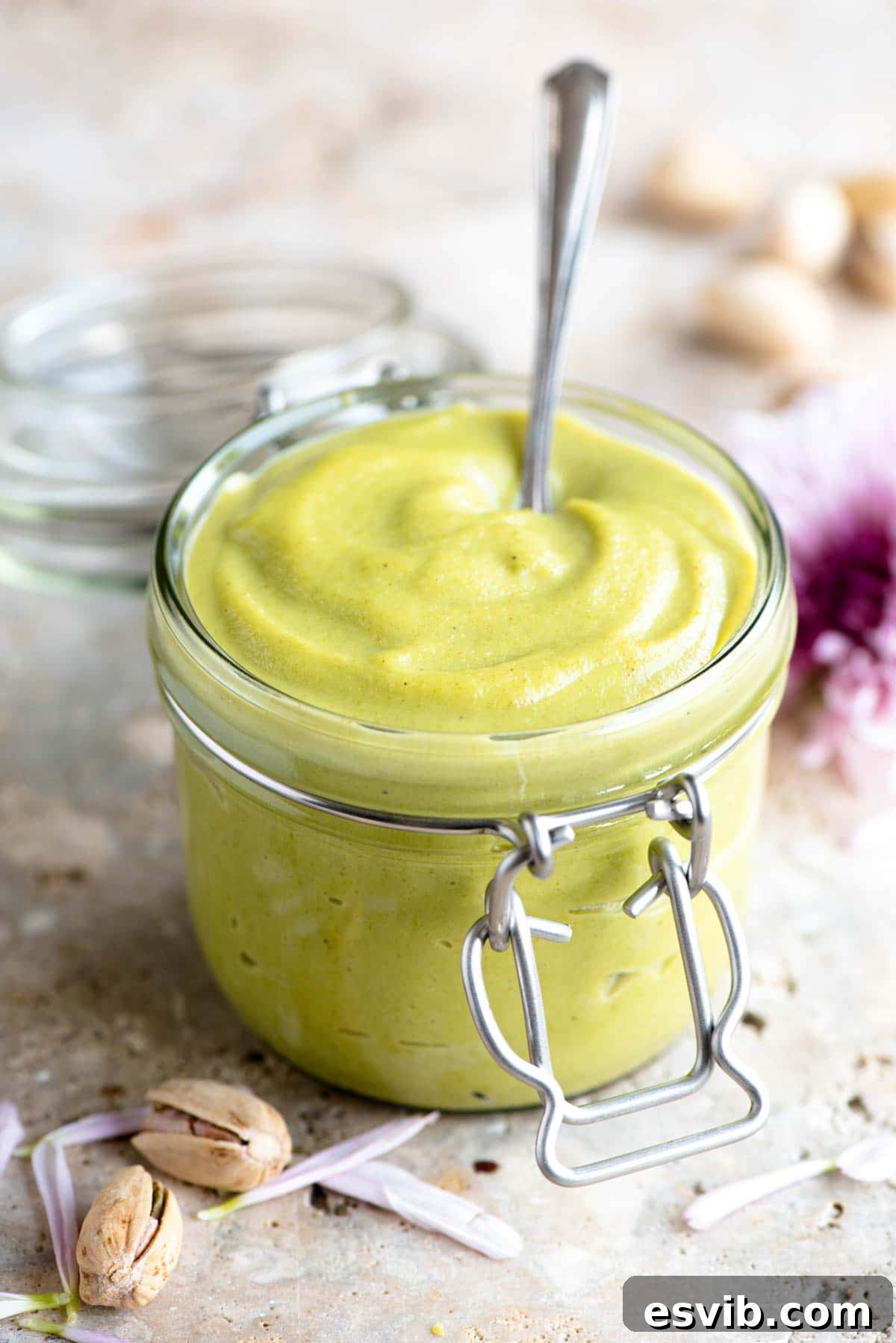 Velvety Italian Pistachio Cream 2 A jar of homemade pistachio cream with a spoon in it, showcasing its vibrant green color and smooth texture.