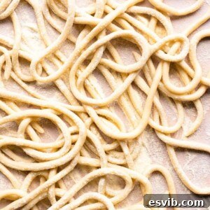 A close up of pici pasta on a neutral background