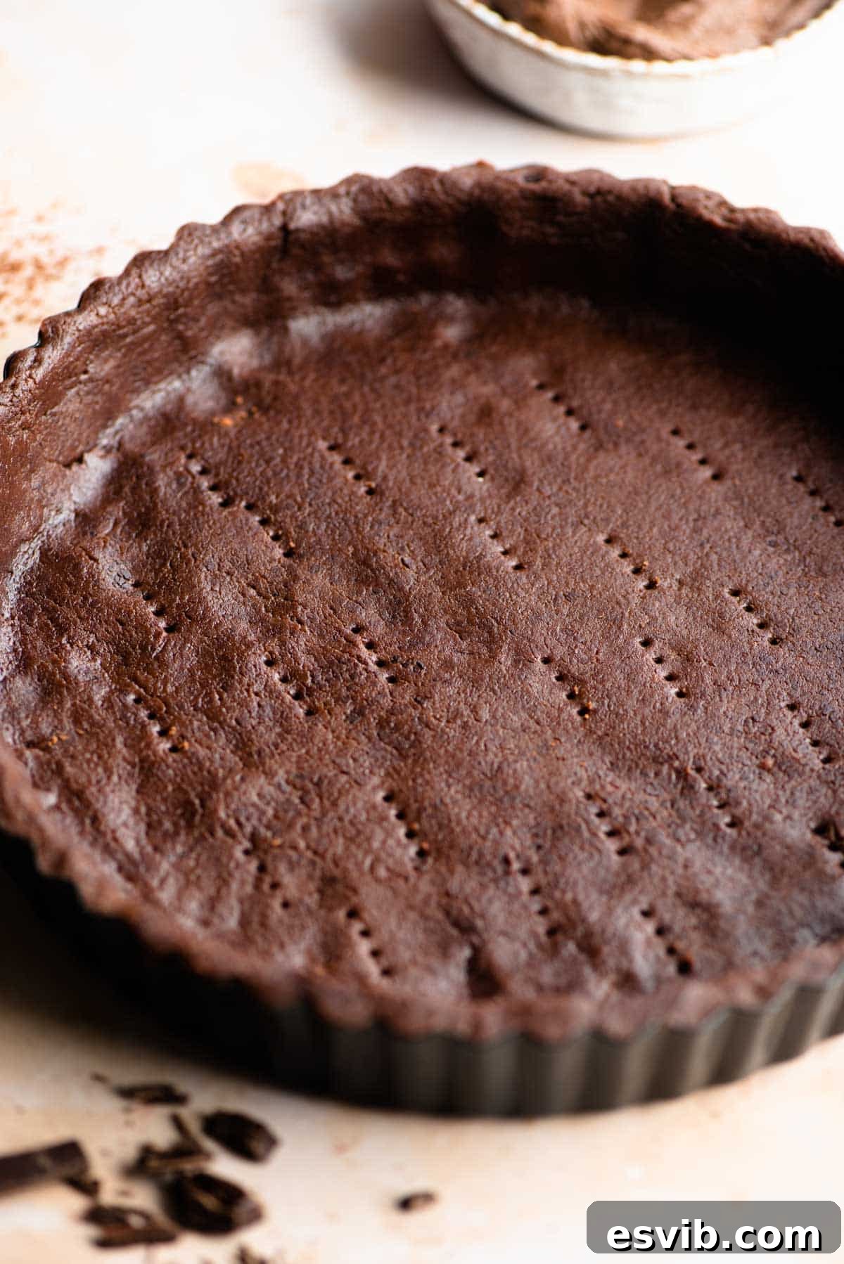 A close up of raw chocolate shortcrust pastry perfectly molded into a tart pan, ready for baking