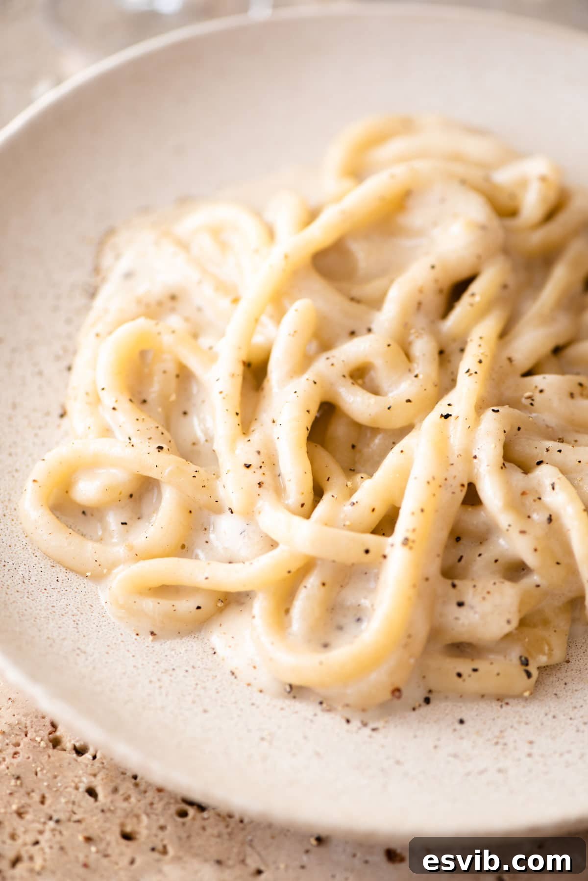 Classic Pici Cacio e Pepe 6 A vibrant close-up of pici pasta coated generously with Cacio e Pepe sauce on a plate, highlighting its creamy texture and distinct black pepper flecks.