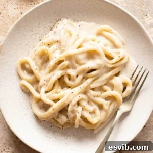 A close up of cacio e pepe with pici pasta on a plate with a fork