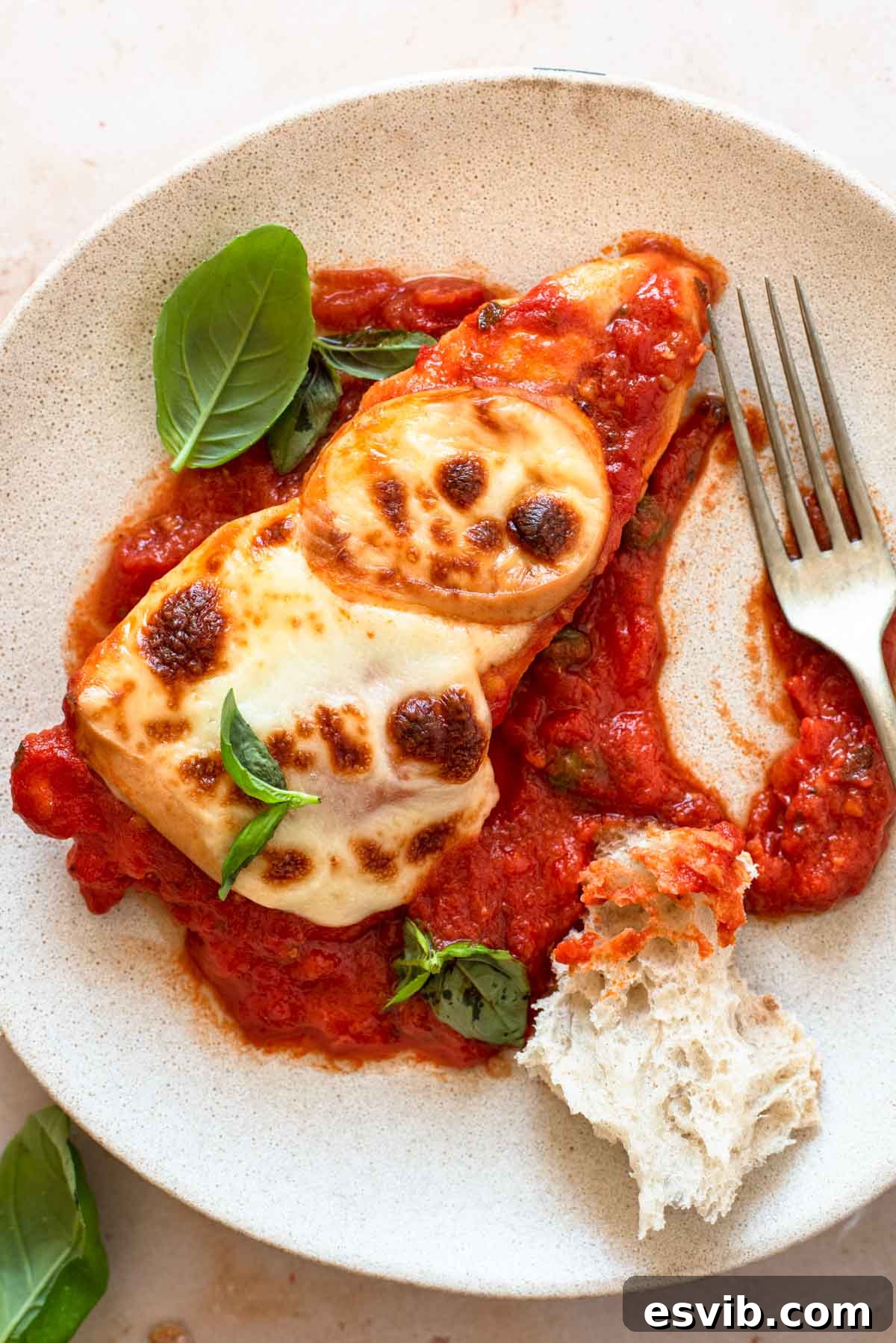 Smoky Scamorza Chicken Pizzaiola 2 A close up of a piece of chicken pizzaola on a plate with crusty bread and basil leaves, showcasing the rich tomato sauce and melted cheese