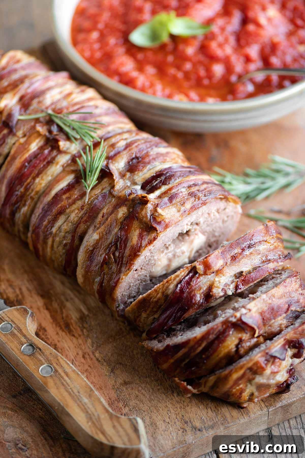 Crispy Pancetta Italian Meatloaf 2 An Italian meatloaf wrapped in pancetta sitting on a wooden cutting board with some slices cut, revealing a creamy cheese filling.