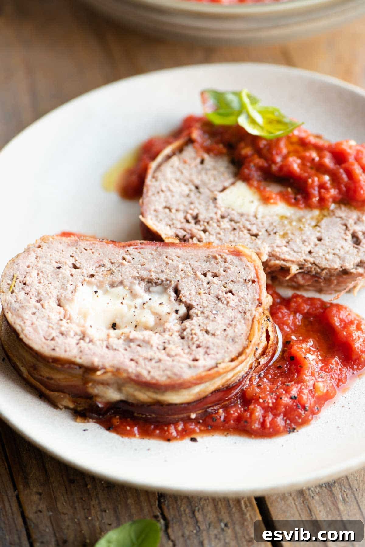 Crispy Pancetta Italian Meatloaf 8 Two generous slices of Italian meatloaf, stuffed with melted cheese and wrapped in crispy pancetta, presented on a plate with a side of rich tomato sauce.
