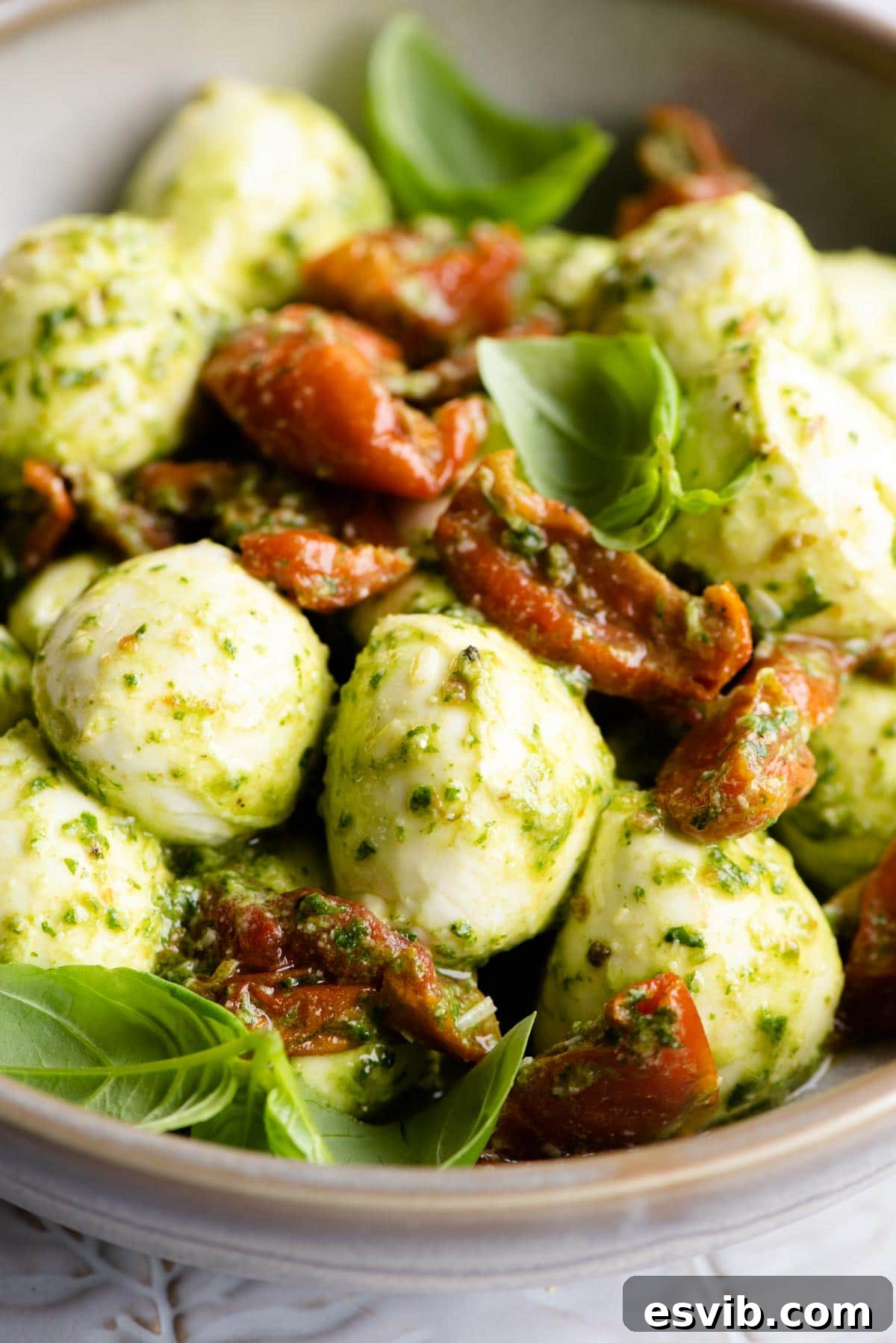 A close-up shot of mozzarella bocconcini balls generously coated with basil pesto and mixed with sun-blushed tomatoes, showcasing the delicious texture.