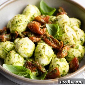 A close up of mozzarella bocconcini in a bowl with pesto and tomatoes