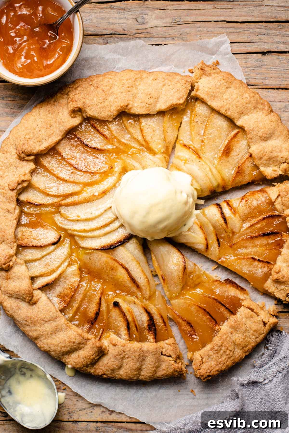 An overhead shot of an apple crostata with some slices cut and a scoop of ice cream on top, ready to be served