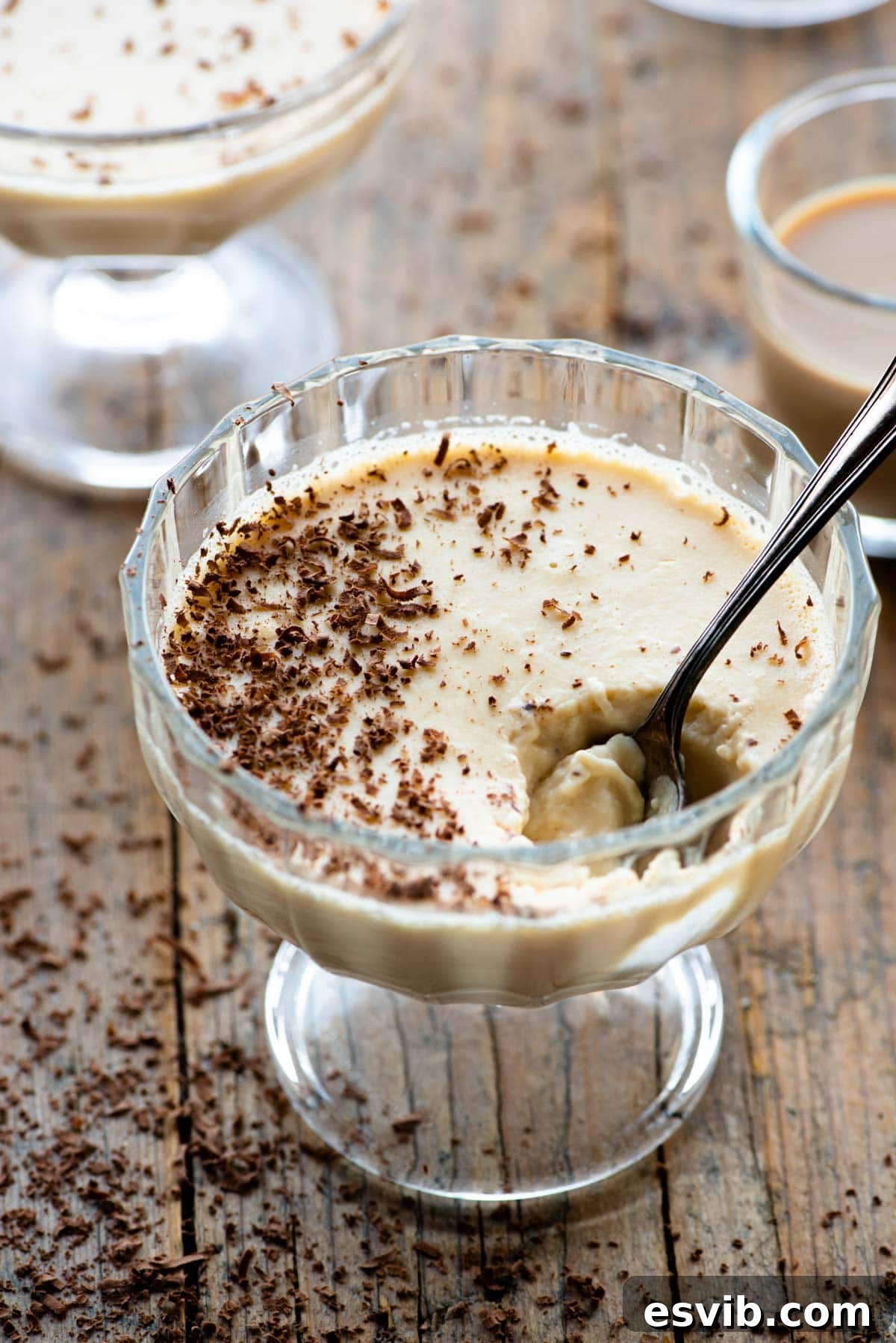 Bailey's Velvet Panna Cotta 2 A small glass dish filled with creamy Bailey's Panna Cotta, garnished with grated dark chocolate and a spoon resting nearby.