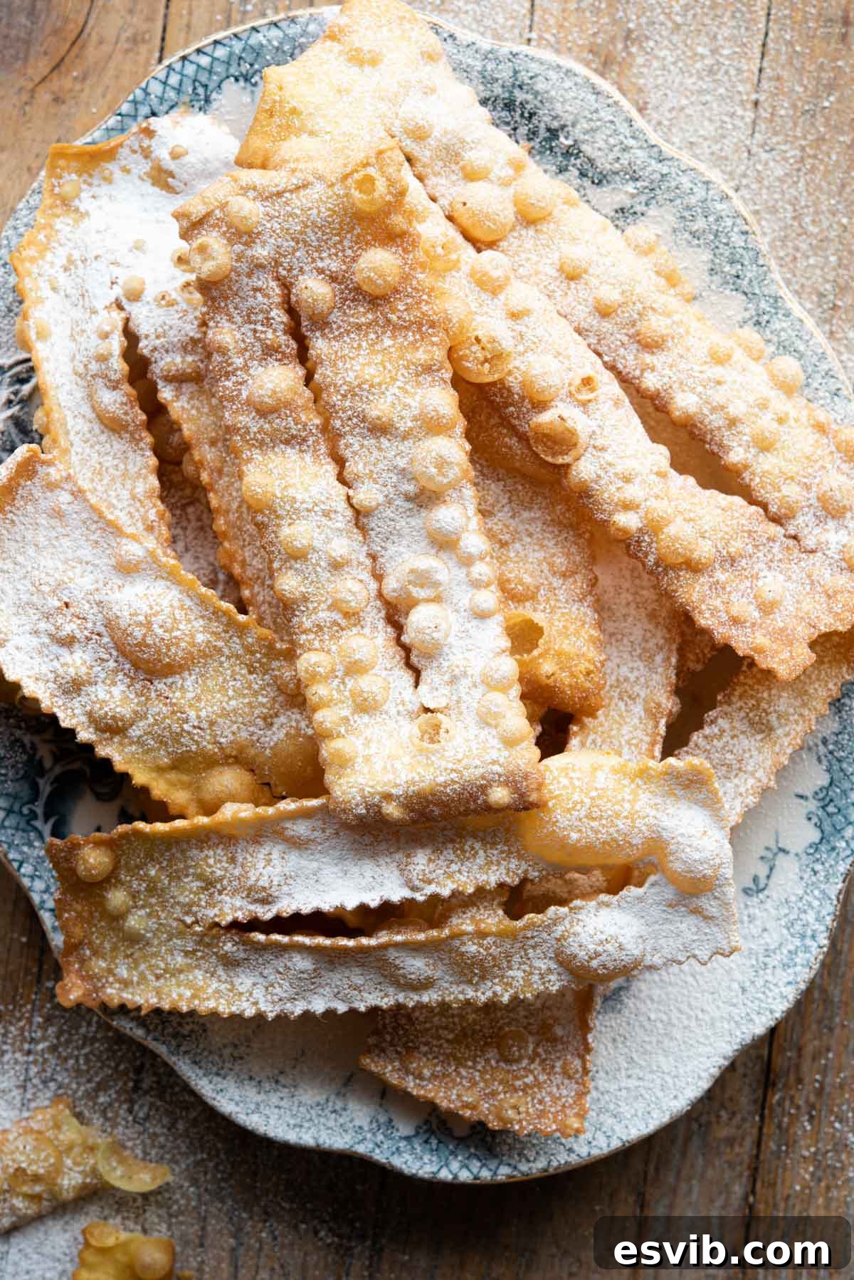 Italian Carnival Ribbons: Golden Fried Delights 2 An overhead shot of Cenci Italian pastries on a blue plate, generously dusted with powdered sugar.