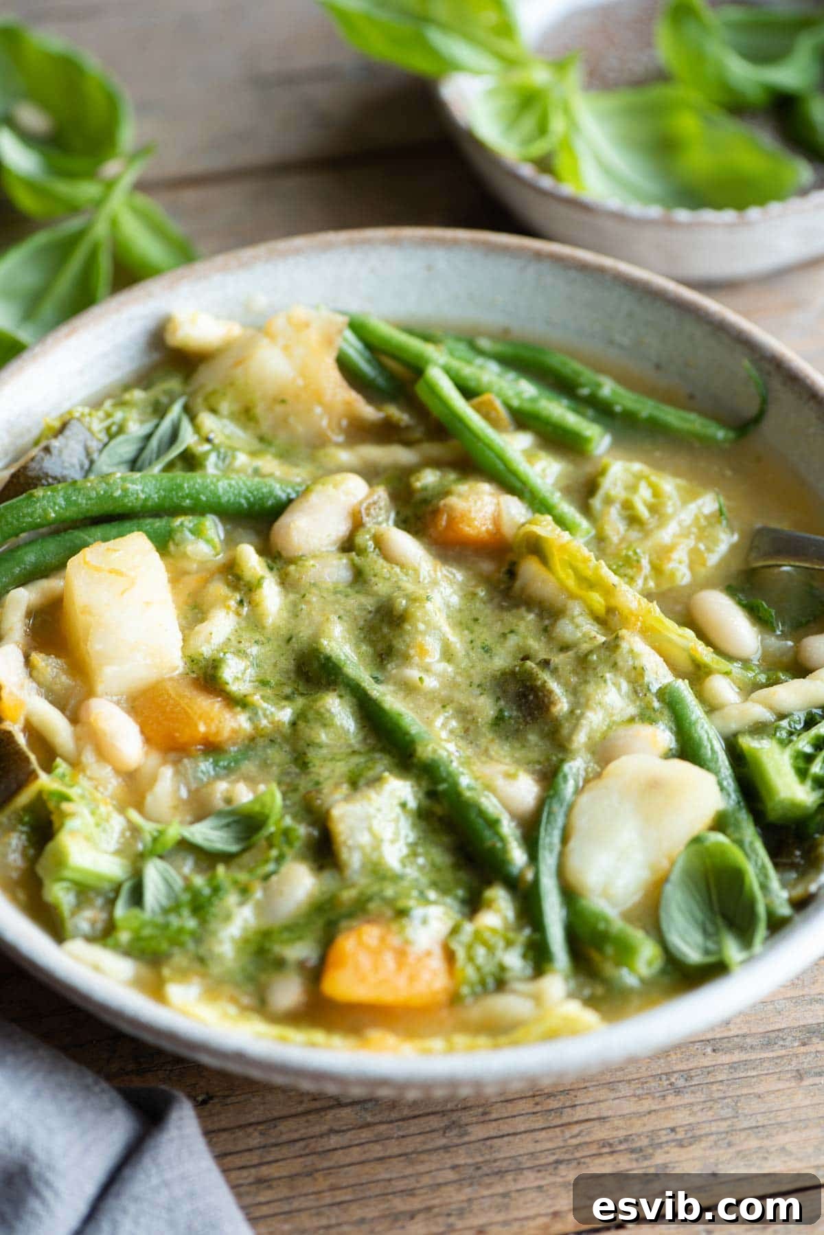 A vibrant close-up of a bowl of Ligurian minestrone soup, showcasing a rich medley of mixed vegetables like squash, zucchini, and beans, topped with a bright green swirl of basil pesto. The texture of the soup is inviting, highlighting the wholesome ingredients.