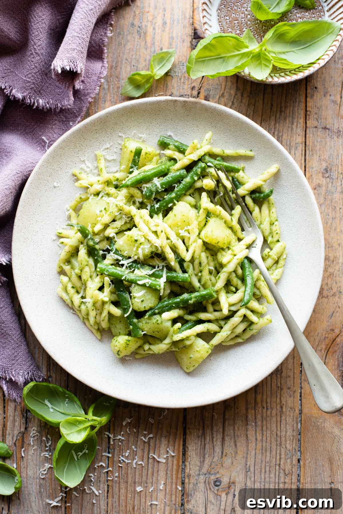 A vibrant plate of Trofie pasta with fresh pesto, tender potatoes, and crisp green beans, beautifully arranged on a rustic wooden surface, highlighting the dish's visual appeal.