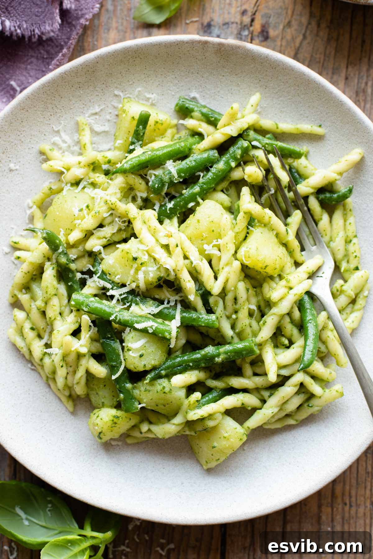 A close-up shot of the exquisite Trofie pasta dish, generously coated with fresh pesto and interspersed with tender potatoes and vibrant green beans, presented on a plate with a fork resting beside it, inviting a taste.