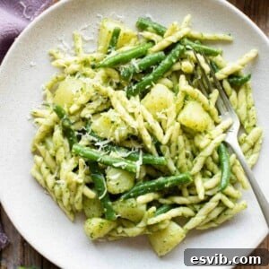 A close up of pesto pasta on a plate with potatoes and green beans