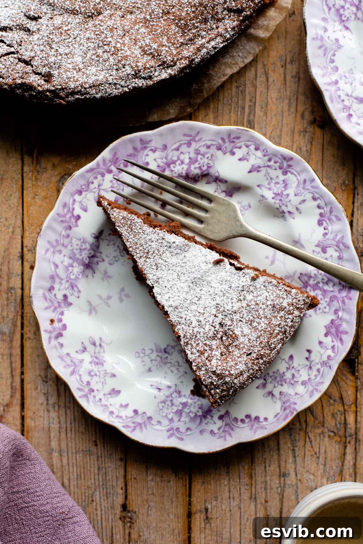 Torta Caprese: Decadent Flourless Italian Chocolate Torte 2 An overhead shot of a perfectly sliced chocolate Torta Caprese resting on a charming pink patterned plate, elegantly dusted with powdered sugar, ready to be served and savored.