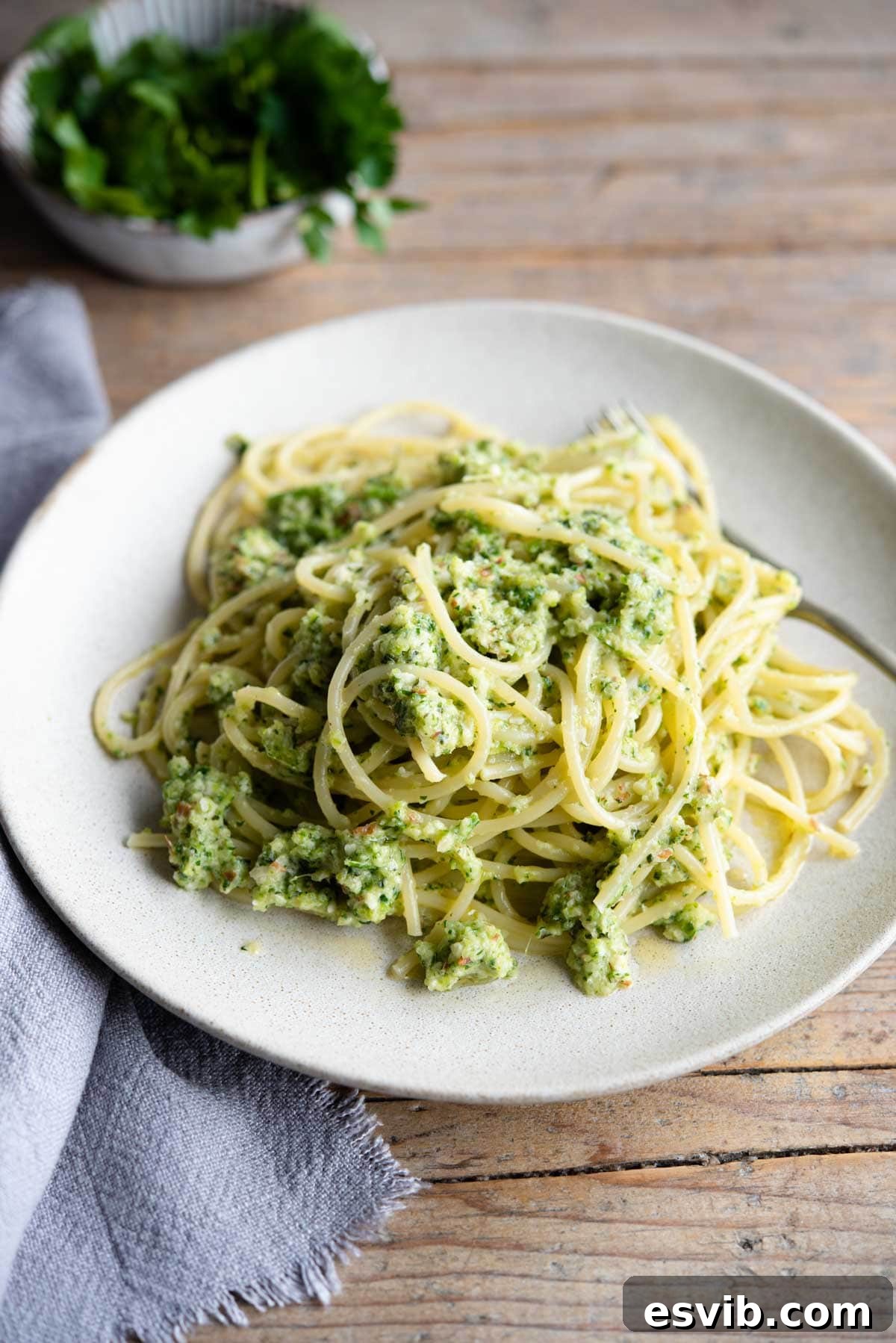 A plate of freshly prepared zucchini pesto pasta on a wooden surface, garnished with a blue kitchen towel