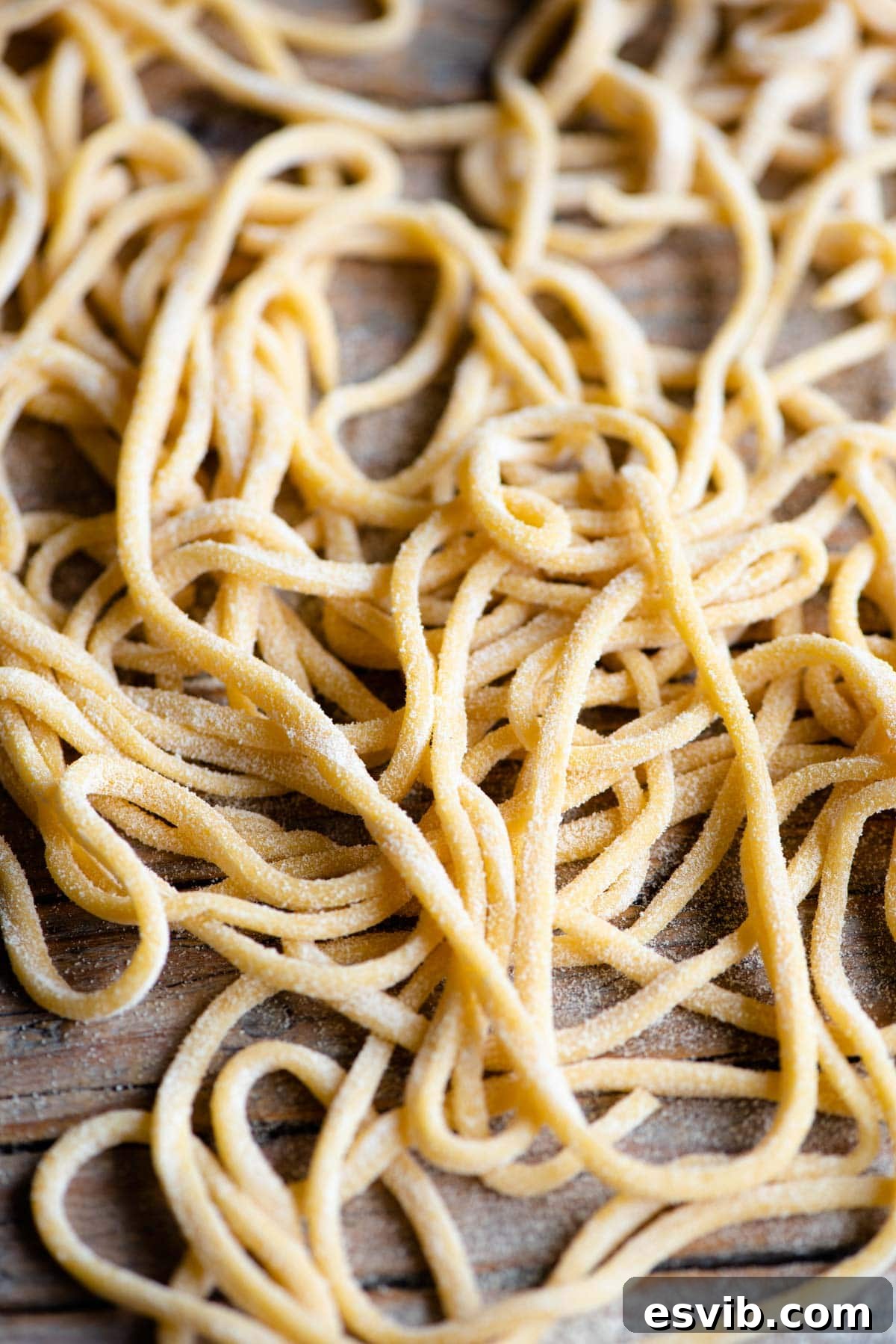 Homemade Tonnarelli Pasta 9 A close-up of Tonnarelli pasta, also known as Spaghetti alla Chitarra, scattered on a rustic wooden surface, highlighting its square edges and texture.