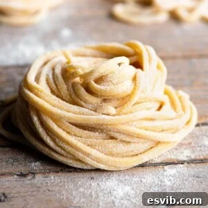 A close-up of Tonnarelli pasta rolled into a nest sitting on a rustic wooden surface, showcasing its fresh texture.
