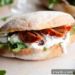 A close up of a ciabatta sandwich filled with arugula, burrata, anchovies and tomatoes, highlighting its fresh and inviting appearance.