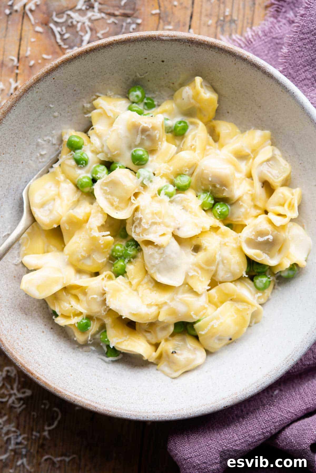An overhead shot of Tortellini in a bowl with a cream sauce and peas