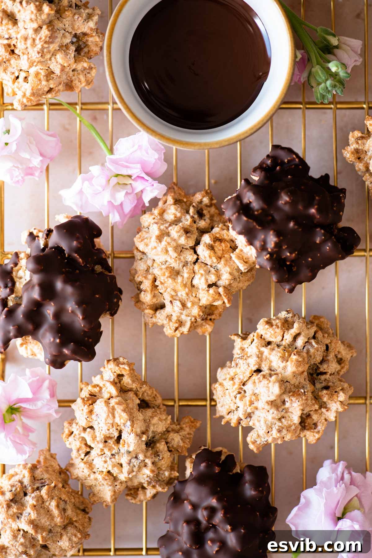 An overhead shot of both original and chocolate Brutti ma Buoni cookies on a gold cooling rack with pink flowers dotted around, showcasing their rustic charm.