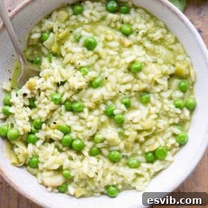 A close up of a bowl of creamy risotto with vibrant green pesto swirls and whole peas, garnished with fresh basil leaves.
