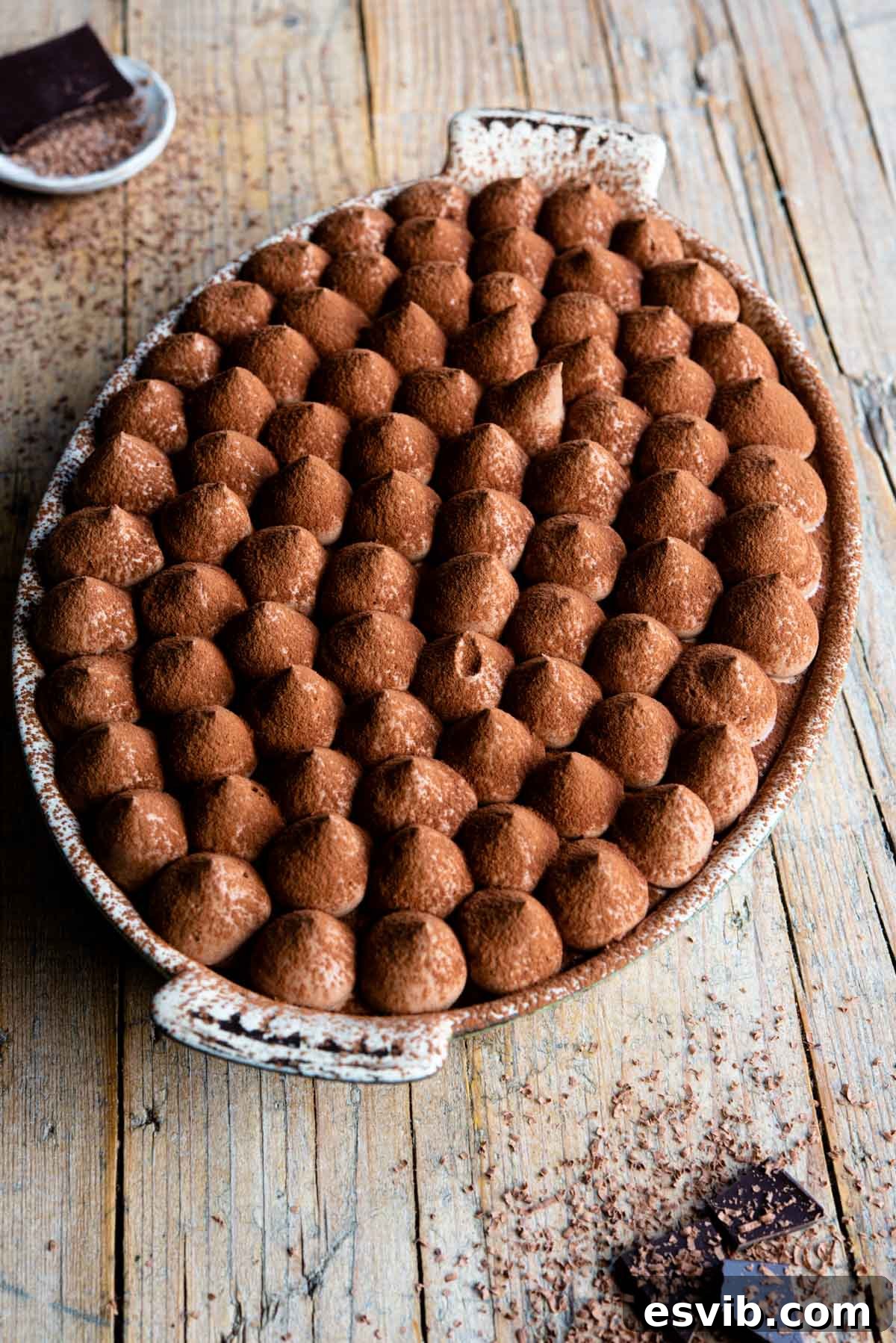 A stunning Chocolate Tiramisu in an elegant oval dish, resting on a rustic wooden background with decorative pieces of dark chocolate on the side.