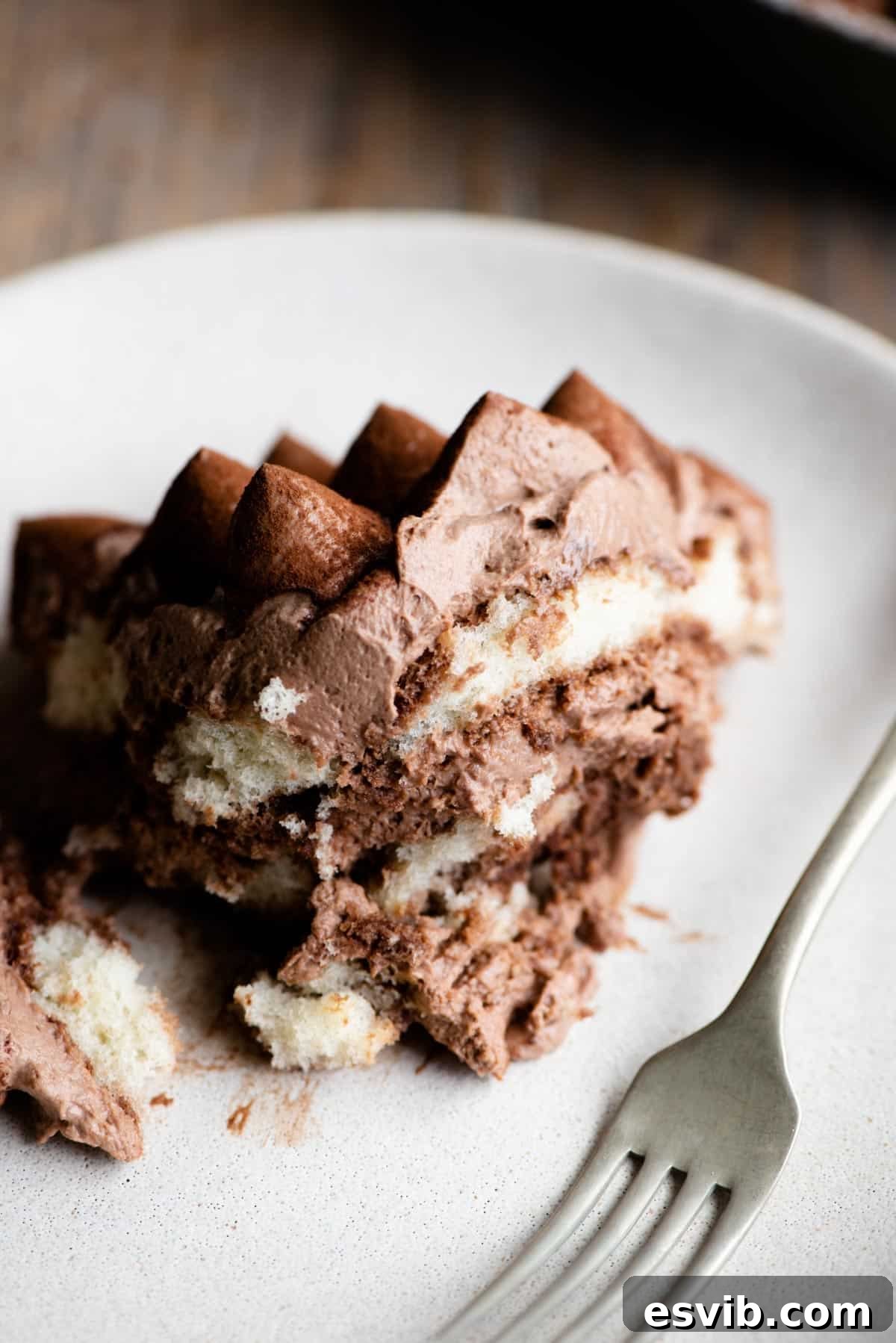 A close-up view of a perfectly portioned piece of chocolate tiramisu resting on a light-colored plate, accompanied by a fork, ready to be enjoyed.