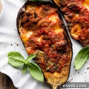 A close-up of half a stuffed eggplant on a plate, beautifully topped with fresh basil, showcasing its melted mozzarella and rich filling.