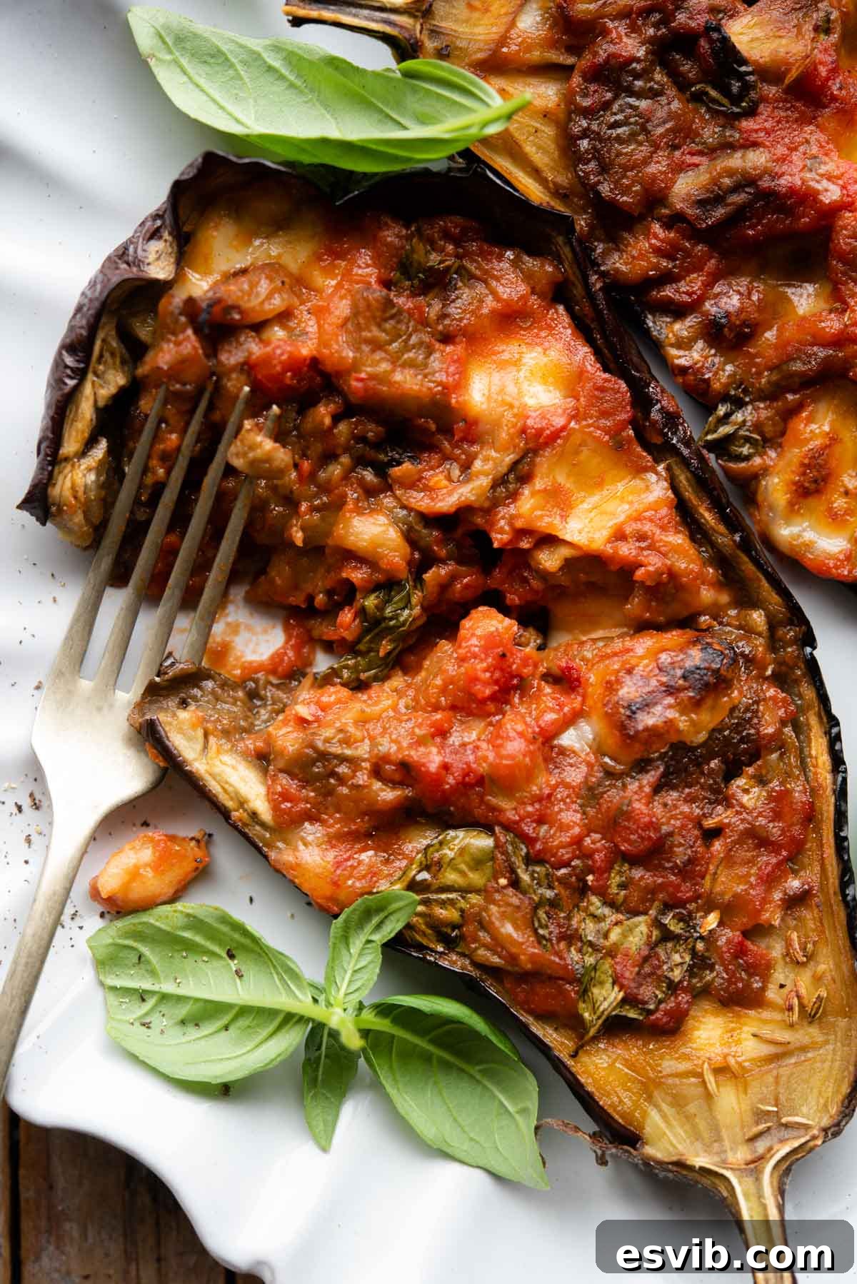 A truly delectable close-up of a halved Italian stuffed eggplant, revealing its rich, vibrant tomato and melted mozzarella filling, elegantly served on a plate and garnished with a sprig of fresh basil.