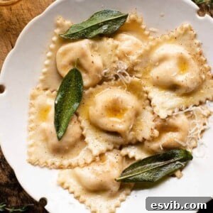 A cropped square image of butternut squash ravioli in a bowl with sage leaves and brown butter sauce.