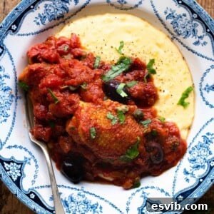 A cropped close-up of chicken puttanesca with creamy polenta in a blue bowl, garnished with fresh parsley.