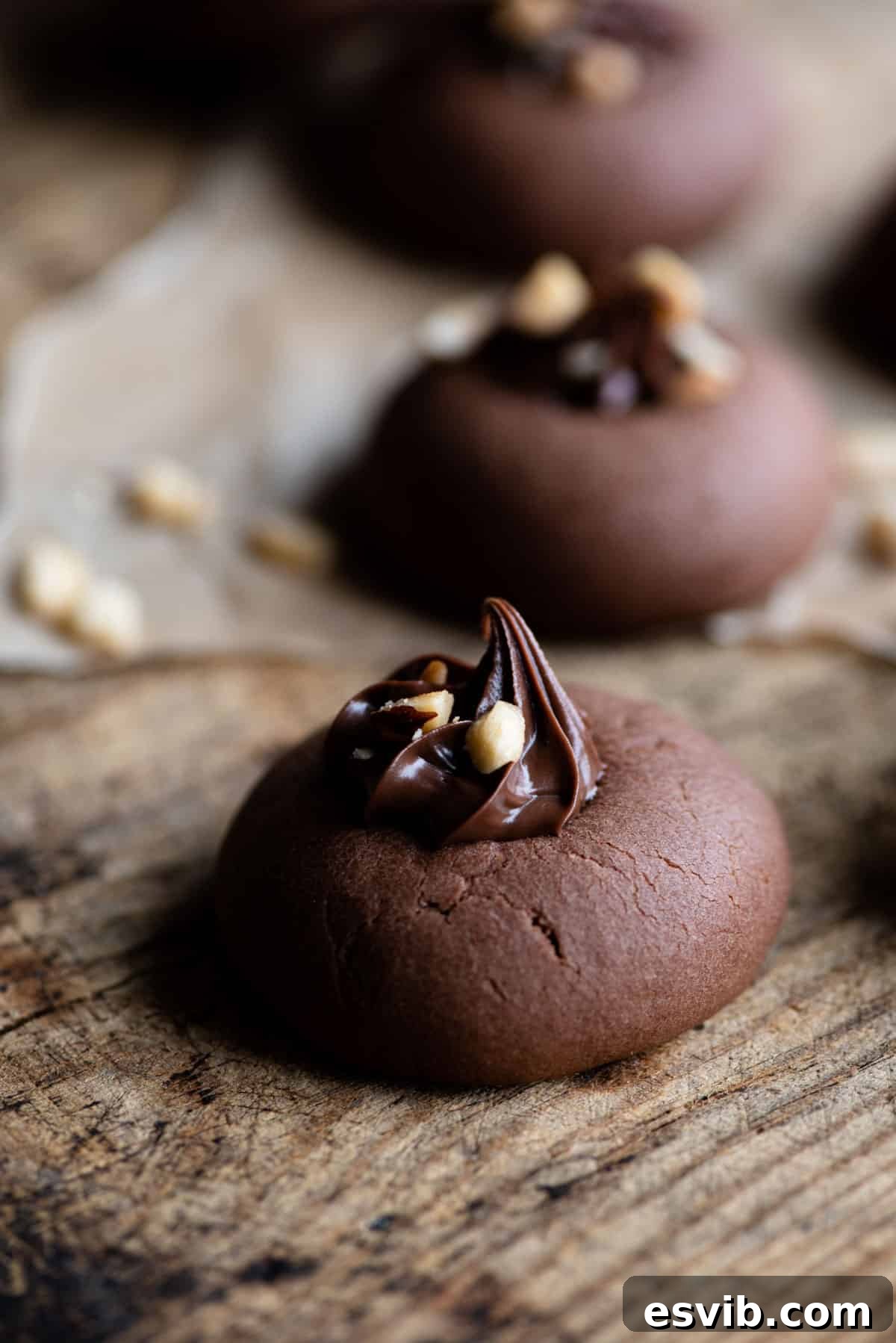 A close-up side shot of a single Italian Nutella cookie, perfectly topped with a swirl of Nutella and sprinkled with chopped hazelnuts, showcasing its soft texture.