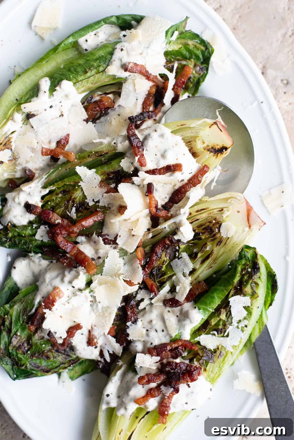 An overhead shot of grilled romaine lettuce generously topped with crispy pancetta and a creamy caper dressing, ready to be served.